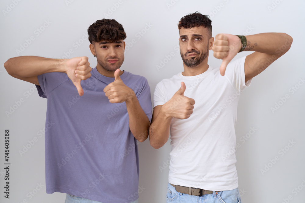 Homosexual gay couple standing over white background doing thumbs up and down, disagreement and agreement expression. crazy conflict Homosexual gay couple standing over white background doing thumbs up and down, disagreement and agreement expression. crazy conflict