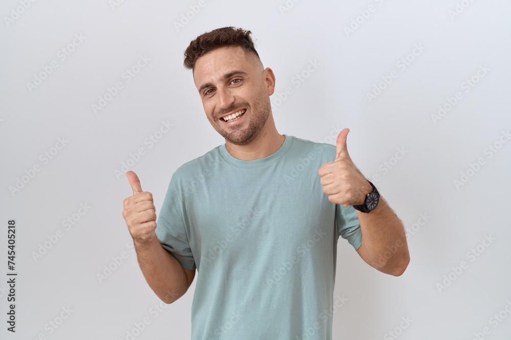 Hispanic man with beard standing over white background success sign doing positive gesture with hand, thumbs up smiling and happy. cheerful expression and winner gesture. Hispanic man with beard standing over white background success sign doing positive gesture with hand, thumbs up smiling and happy. cheerful expression and winner gesture.