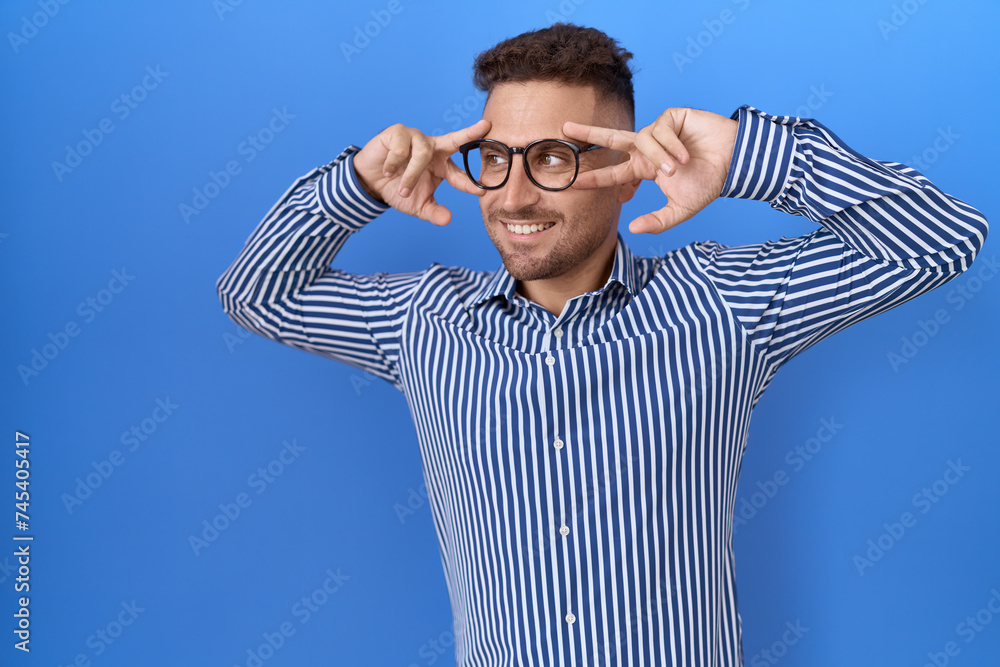 Hispanic man with beard wearing glasses doing peace symbol with fingers over face, smiling cheerful showing victory Hispanic man with beard wearing glasses doing peace symbol with fingers over face, smiling cheerful showing victory
