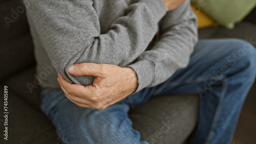 Photography A middle-aged man with grey hair experiencing elbow pain at home, conveying a sense of discomfort