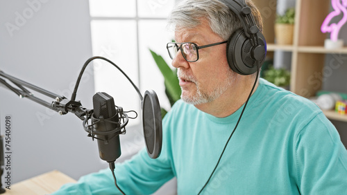 Fotografie Mature man with headphones speaks into a microphone in a radio studio, portraying a professional atmosphere