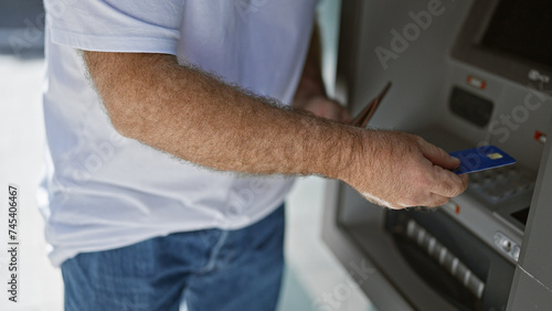 Attractive middle-aged caucasian man inserting credit card into street atm machine in urban city - a handsome, bearded adult in finance service, engaging in outdoor banking transaction.