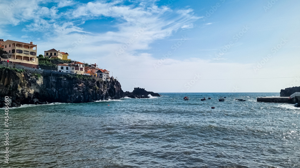 Panoramic view of colourful houses build on steep cliffs in fishermen village of Camara de Lobos on Madeira island, Portugal, Europe. Calm water surface on Atlantic Ocean. Travel destination seascape