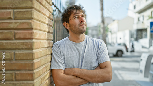 Cheerful young man, standing on an urban street, flashing a confident smile with his arms crossed