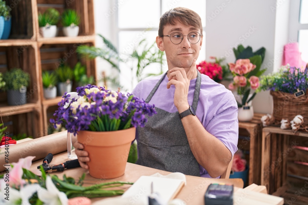 Caucasian blond man working at florist shop thinking worried about a question, concerned and nervous with hand on chin