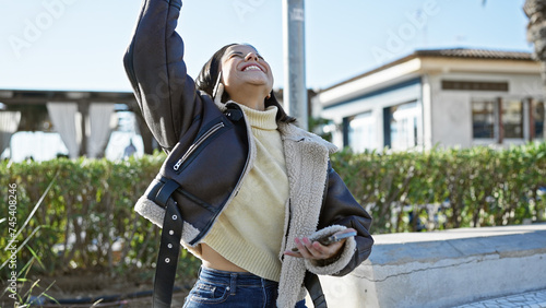 A joyful young hispanic woman enjoys the outdoors, smiling euphorically in a sunny park. photo