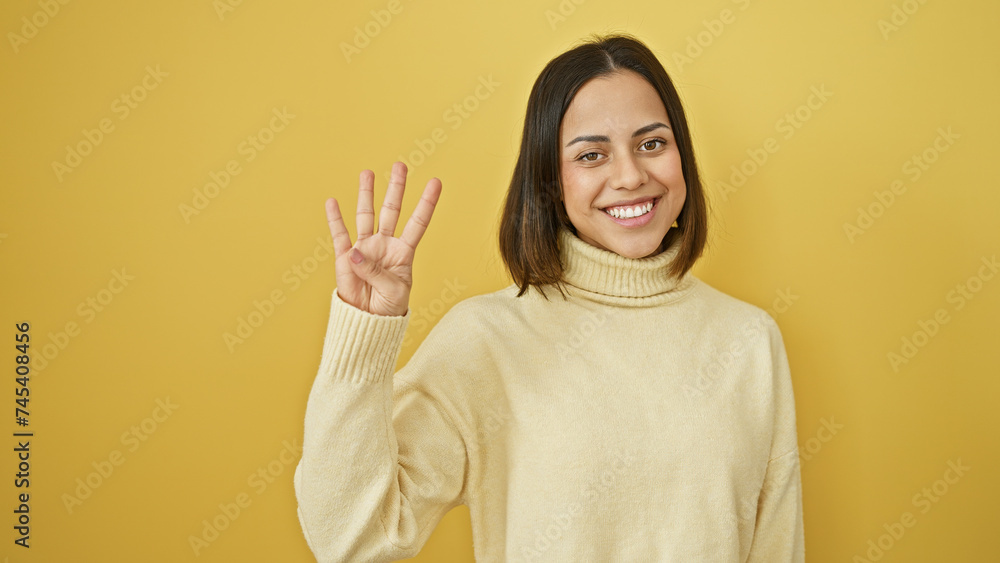 Fototapeta premium Smiling young hispanic woman posing against a yellow isolated background, cheerfully gesturing four with her hand
