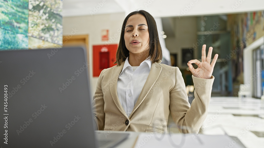 A young hispanic woman meditates while using a laptop in an isolated yellow background setting. A young hispanic woman meditates while using a laptop in an isolated yellow background setting.