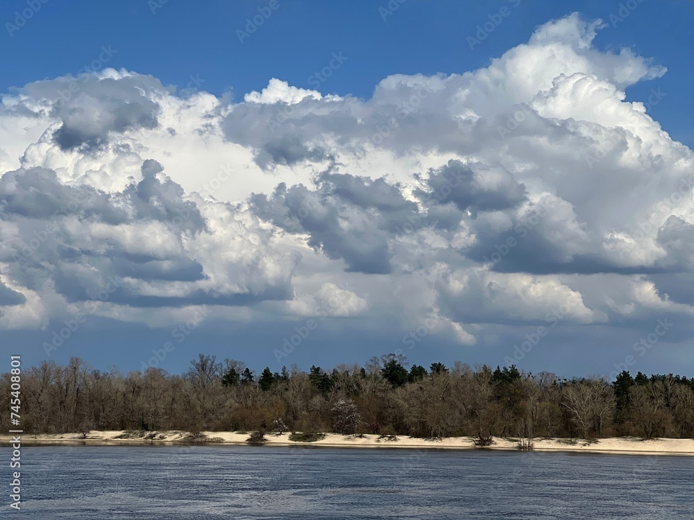 Dramatic sky clouds above river and forest at spring