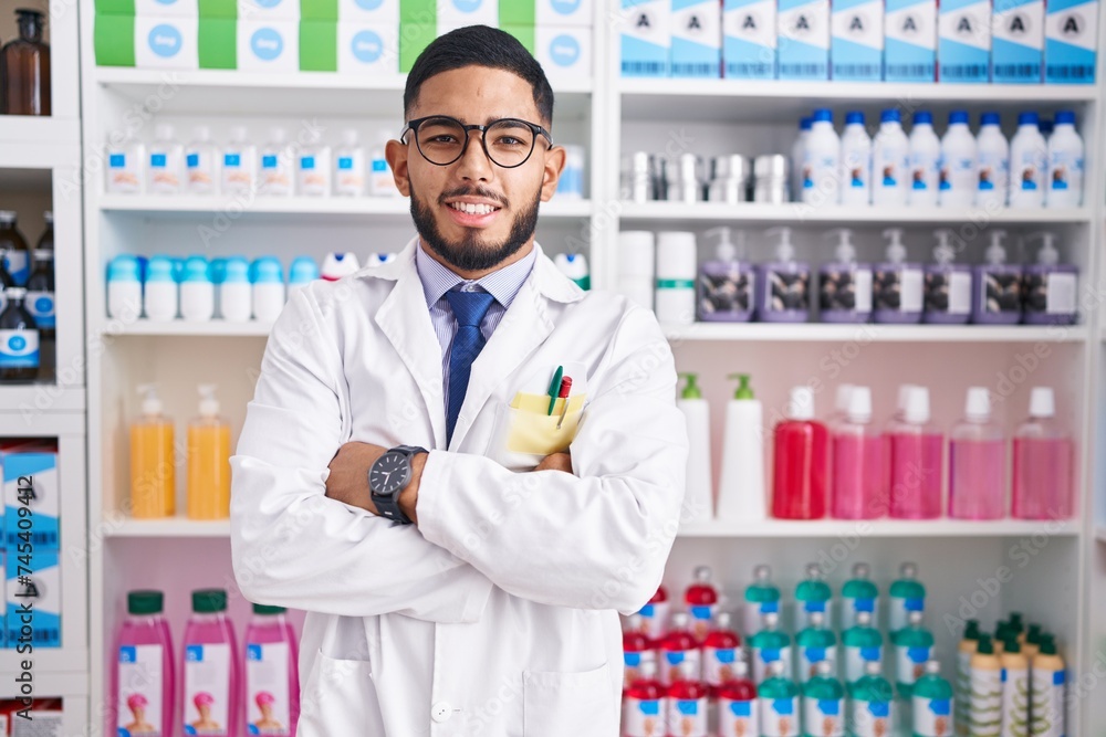 Young latin man pharmacist smiling confident standing with arms crossed gesture at pharmacy