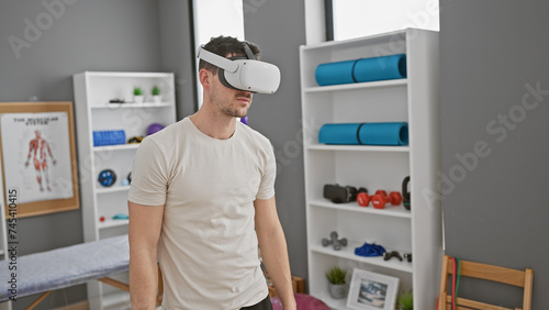 Handsome hispanic man wearing virtual reality headset in modern physiotherapy clinic photo