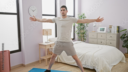 Handsome young man stretching arms in spacious bedroom interior