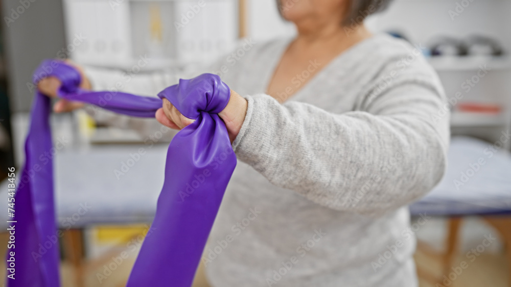 A senior woman exercises with a purple band in the rehabilitation clinic.