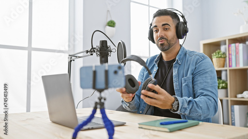 Foto Hispanic man with beard hosting podcast in modern studio, laptop and microphone on table