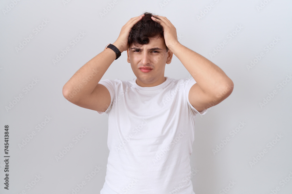 Young non binary man wearing casual white t shirt suffering from headache desperate and stressed because pain and migraine. hands on head. Young non binary man wearing casual white t shirt suffering from headache desperate and stressed because pain and migraine. hands on head.
