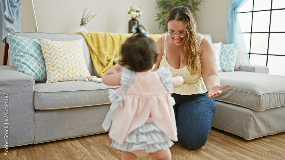 Fototapeta premium Warm mother-daughter duo smiling and exuding confidence in their lovely home, joyfully huddled on the living room sofa - a delightful expression of casual, positive family lifestyle indoors.
