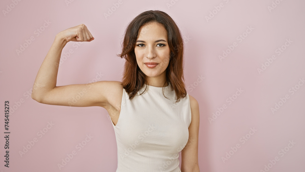 Confident young hispanic woman flexing arm muscles against a soft pink background, portraying strength and femininity. Confident young hispanic woman flexing arm muscles against a soft pink background, portraying strength and femininity.