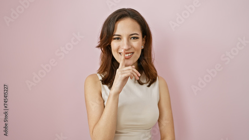 Portrait of a beautiful hispanic woman with a secret gesture, isolated against a pink background.