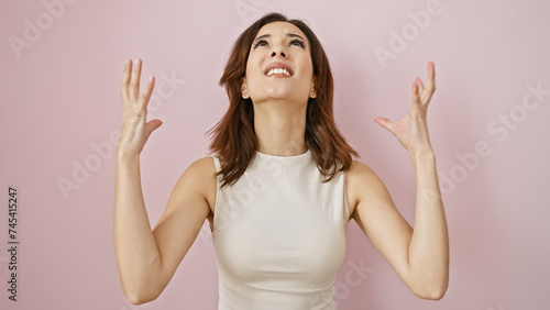 A young hispanic woman looks upwards with a joyful expression, against a pink isolated background.