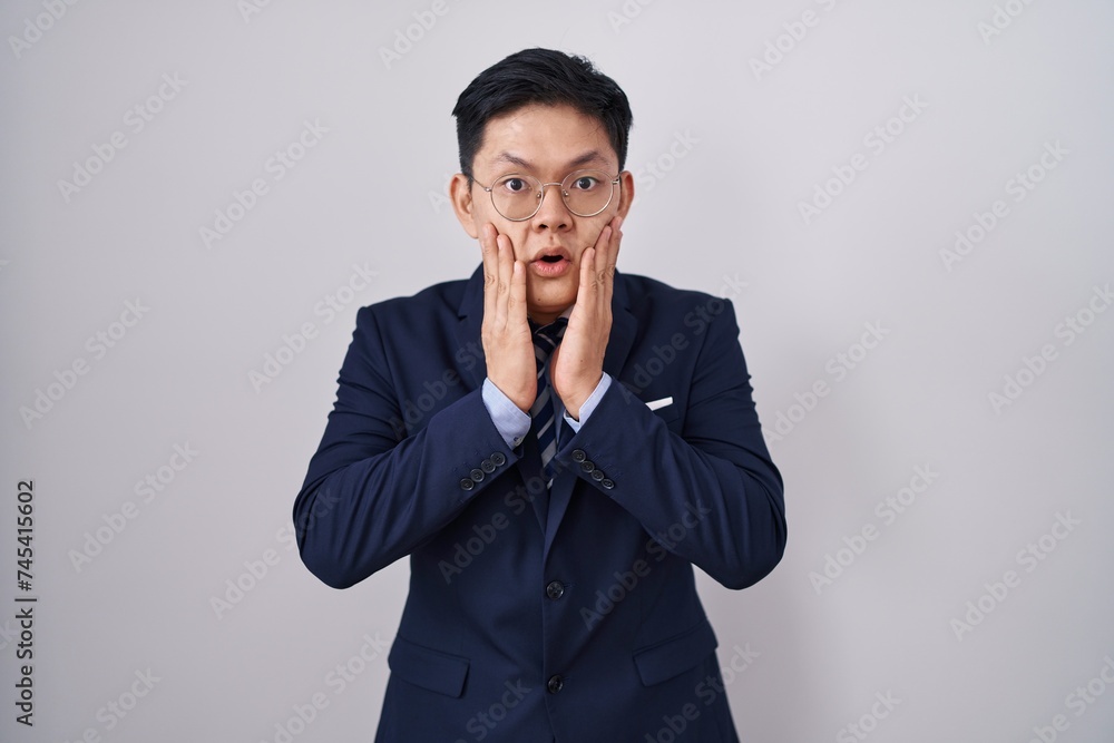 Young asian man wearing business suit and tie afraid and shocked, surprise and amazed expression with hands on face Young asian man wearing business suit and tie afraid and shocked, surprise and amazed expression with hands on face