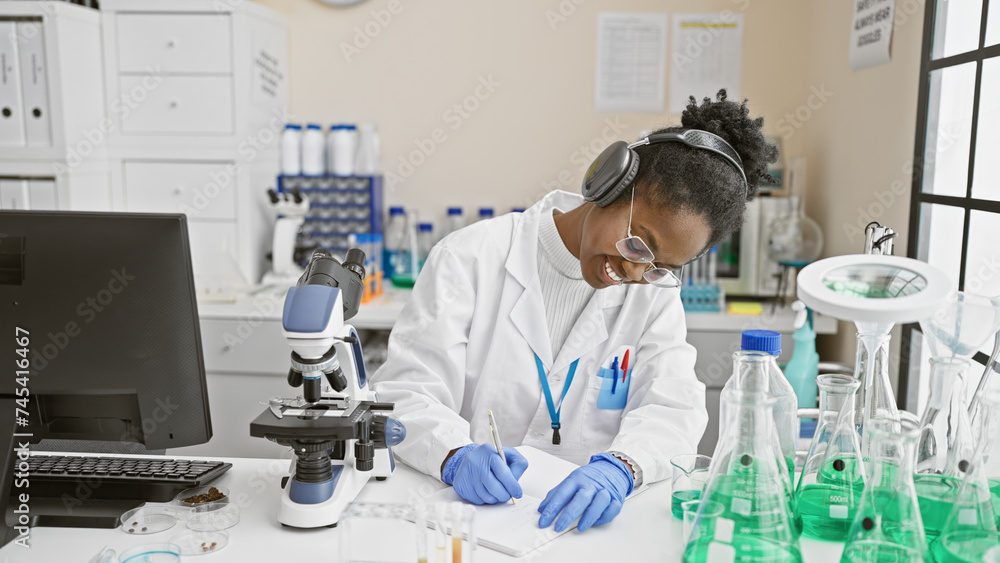 African american woman scientist writing notes in a laboratory with microscope and chemicals African american woman scientist writing notes in a laboratory with microscope and chemicals