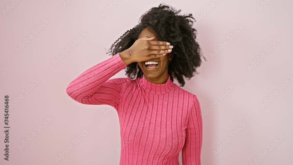 Laughing african woman in pink sweater covering eyes indoors for a playful portrait Laughing african woman in pink sweater covering eyes indoors for a playful portrait