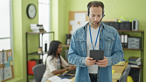 Two workers man and woman using touchpad and headphones working at the office