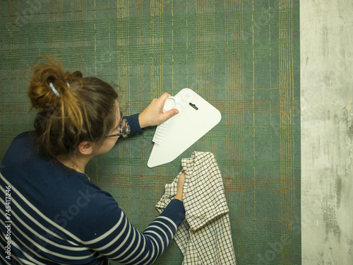 girl gluing wallpaper at home, smoothing out new wallpaper with a plastic spatula