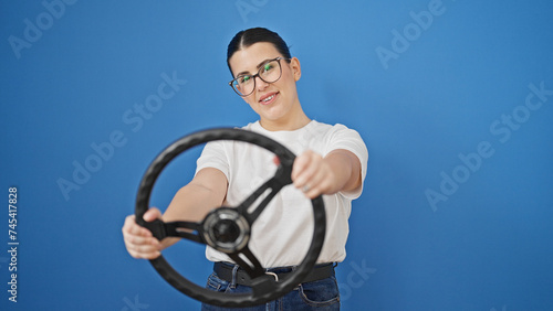 Young beautiful hispanic woman driving using steering wheel over isolated blue background