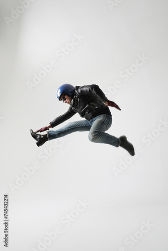 Vertical portrait of young man wearing helmet and black jacket jumping indoor. 