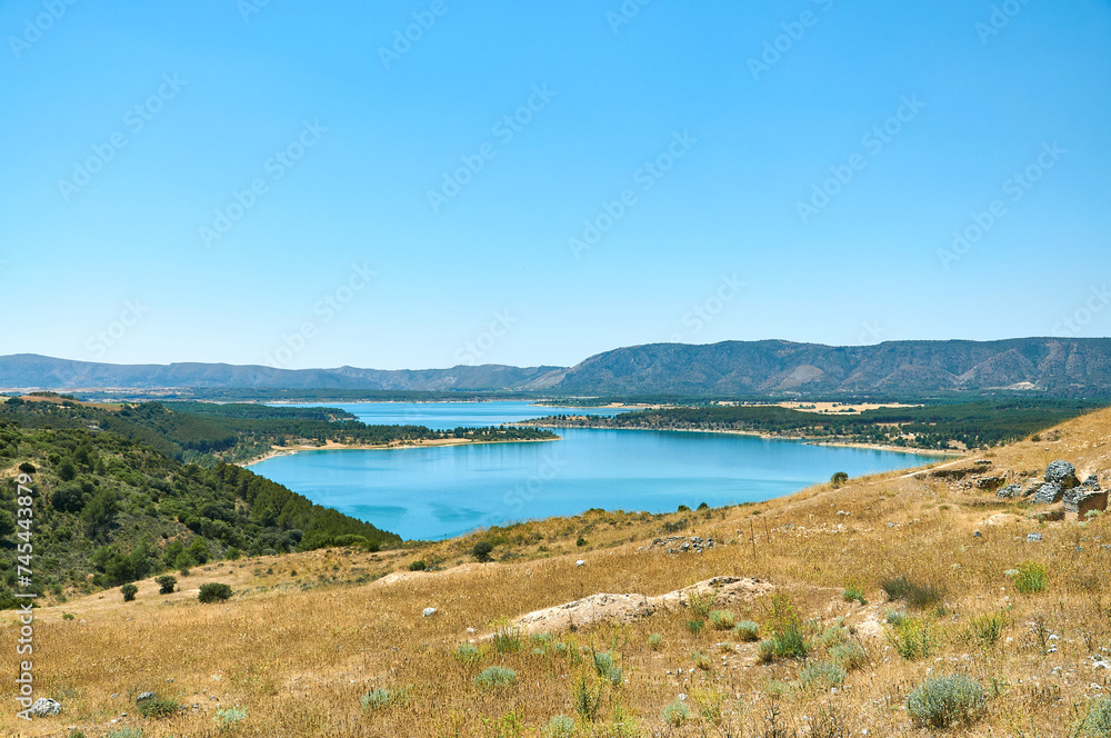 A scenic view featuring vibrant greens, oranges, and the enchanting Buendia reservoir A scenic view featuring vibrant greens, oranges, and the enchanting Buendia reservoir