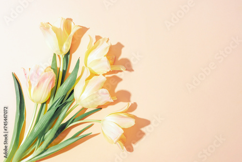 Bouquet of yellow tulips on light peachy background with sharp shadows. Top view  flat lay  copy space