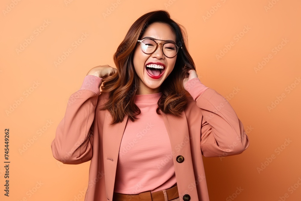 Portrait of a beautiful young asian woman with glasses and coat on orange background