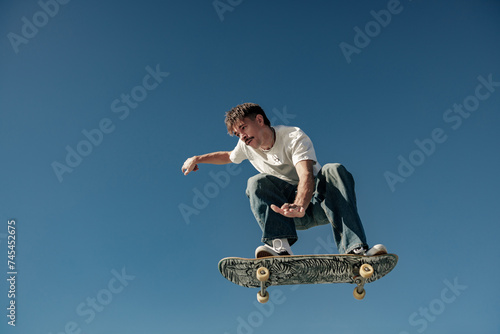 Active man doing tricks in the air on his skateboard at the skate park on blue sky background