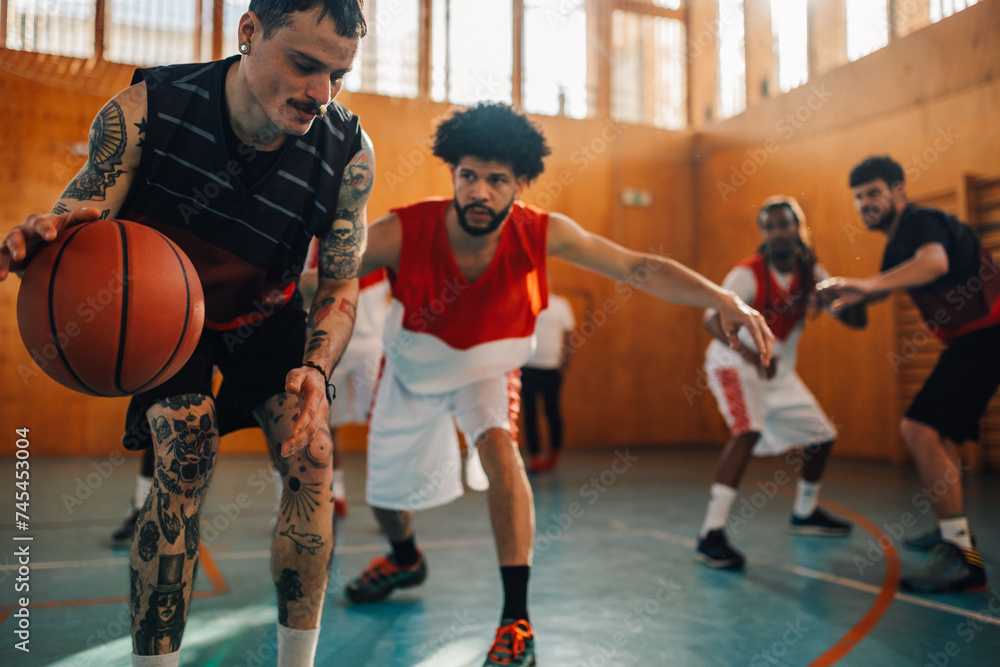 Tattooed hispanic sportsman practicing basketball with his team on court.