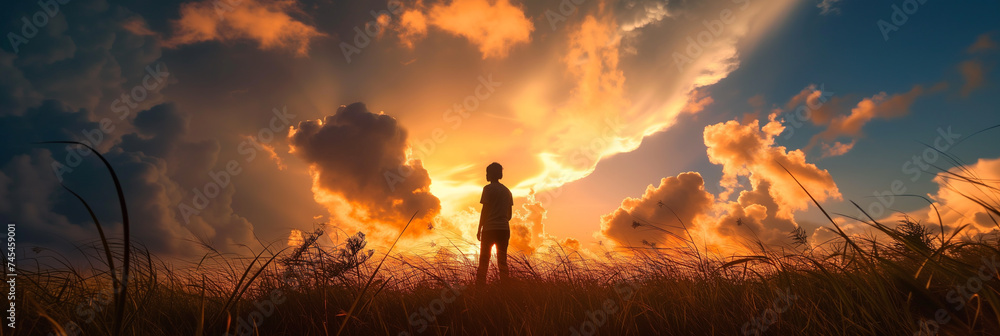 A figure stands in a field, gazing at a dramatic sky with rays of sunlight piercing through clouds.