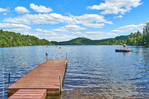 Tranquil lake reflects a vibrant blue sky dotted with fluffy clouds. Long wooden pier stretching into the calm water.
