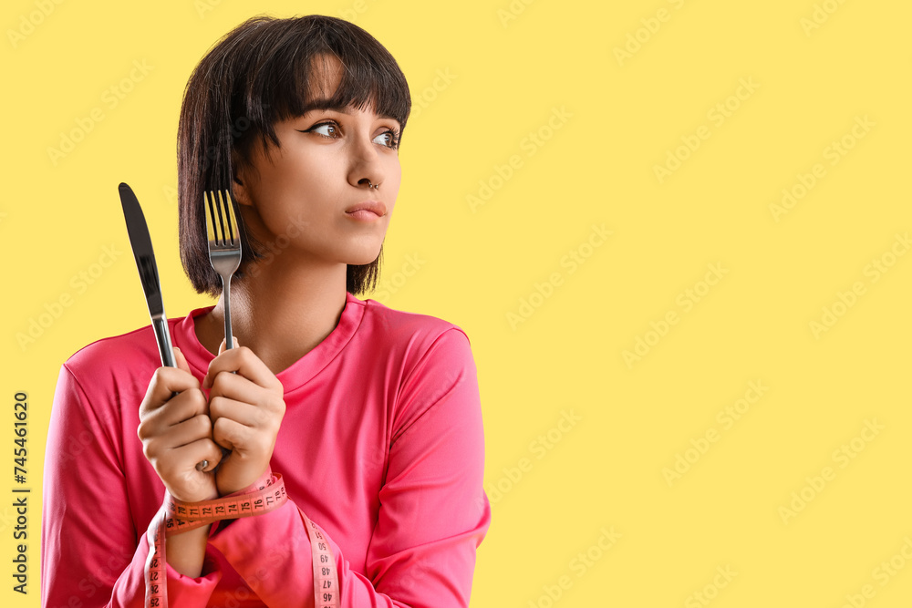 Hungry sporty young woman with cutlery on yellow background, closeup. Diet concept Hungry sporty young woman with cutlery on yellow background, closeup. Diet concept