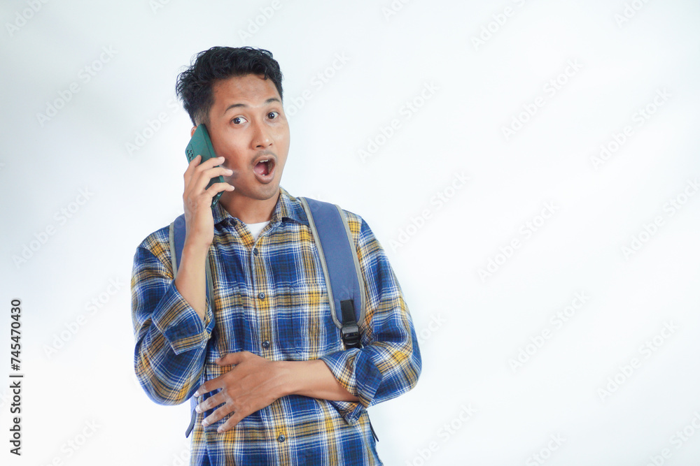 Surprised young Asian man student in casual clothes and backpack glasses talk speak on mobile cell phone with friend isolated on white background. Education in high school university college concept Surprised young Asian man student in casual clothes and backpack glasses talk speak on mobile cell phone with friend isolated on white background. Education in high school university college concept