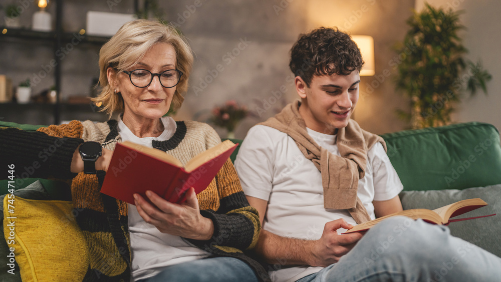 Mother and teenage son man and woman sit at home on sofa bed read book Mother and teenage son man and woman sit at home on sofa bed read book