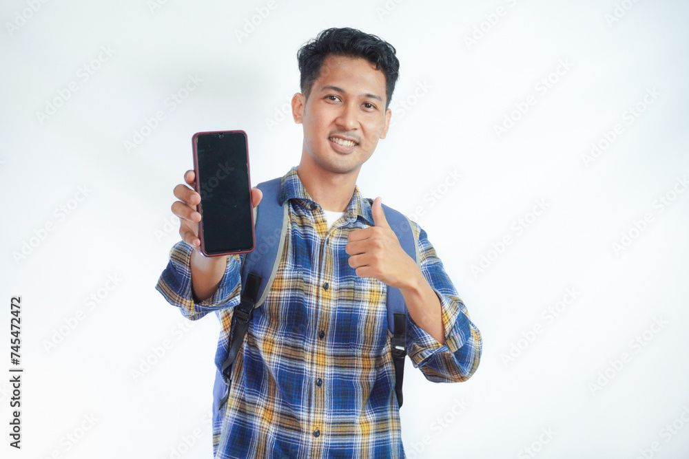 Cheerful young Asian man student in casual clothes backpack showing blank screen smartphone, thumb up gesture, recommends new app isolated on white background. high school university college concept Cheerful young Asian man student in casual clothes backpack showing blank screen smartphone, thumb up gesture, recommends new app isolated on white background. high school university college concept