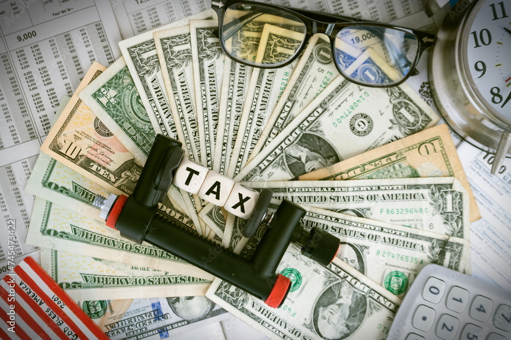 Tax reduction concept. The word TAXES is clamped with a clamp. against the backdrop of dollars and tax tables. Tax reduction concept. The word TAXES is clamped with a clamp. against the backdrop of dollars and tax tables.
