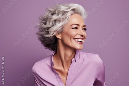 Cheerful mature woman with grey hair. Portrait of beautiful middle-aged woman smiling and looking away while standing against purple background