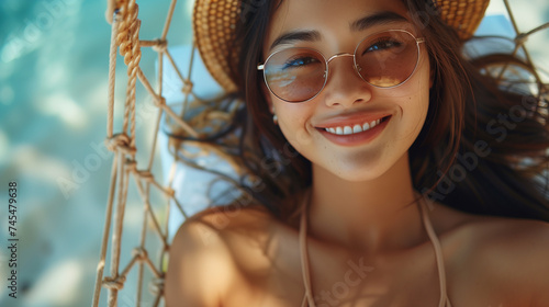 Travel girl tanning lying down relaxing in an outdoor bed hammock on the beach smiling happy sunbathing during summer holidays. Asian woman on tropical island getaway vacation, tropical beach