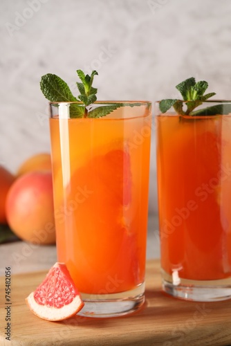 Tasty freshly made grapefruit juice, fruit and mint on table, closeup