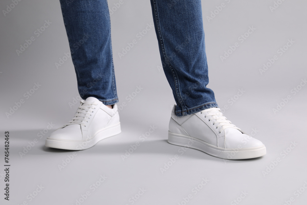 Man wearing stylish white sneakers on grey background, closeup Man wearing stylish white sneakers on grey background, closeup