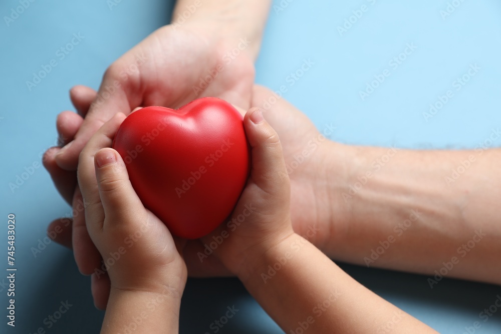 Father and his child holding red decorative heart on light blue background, closeup Father and his child holding red decorative heart on light blue background, closeup