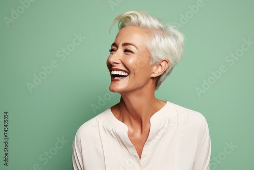 Beautiful middle aged woman laughing and looking at camera isolated over green background