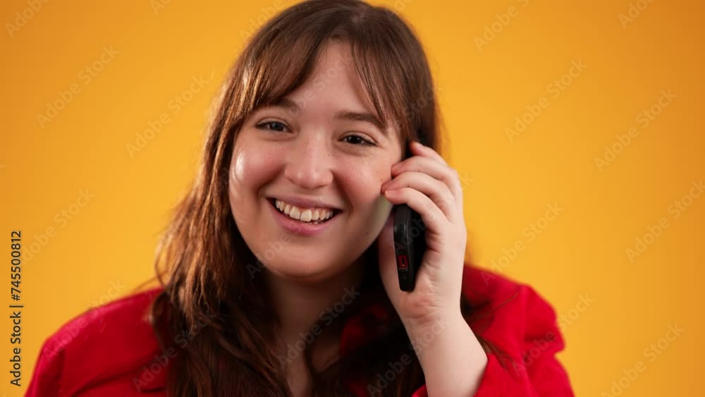 Portrait of happy smiling young woman 20s in red jacket using speaking talking on mobile cell phone conducting pleasant conversation isolated on yellow background studio. Portrait of happy smiling young woman 20s in red jacket using speaking talking on mobile cell phone conducting pleasant conversation isolated on yellow background studio.