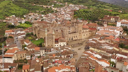 Gothic-Mudejar style building of Royal Monastery of Saint Mary in Spanish town of Guadalupe, located in green valley of province of Caceres overlooking brownish roofs of houses, as seen from drone photo